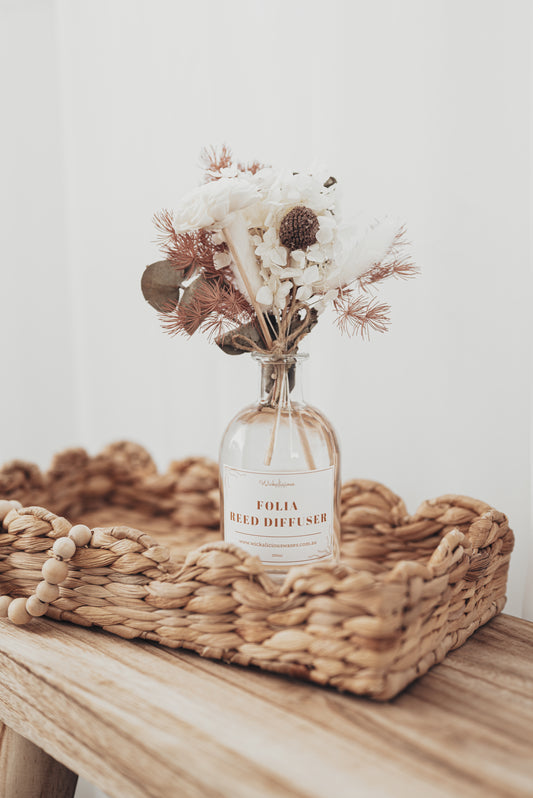 Folia Reed Diffuser in a glass bottle with dried flowers on a woven tray.